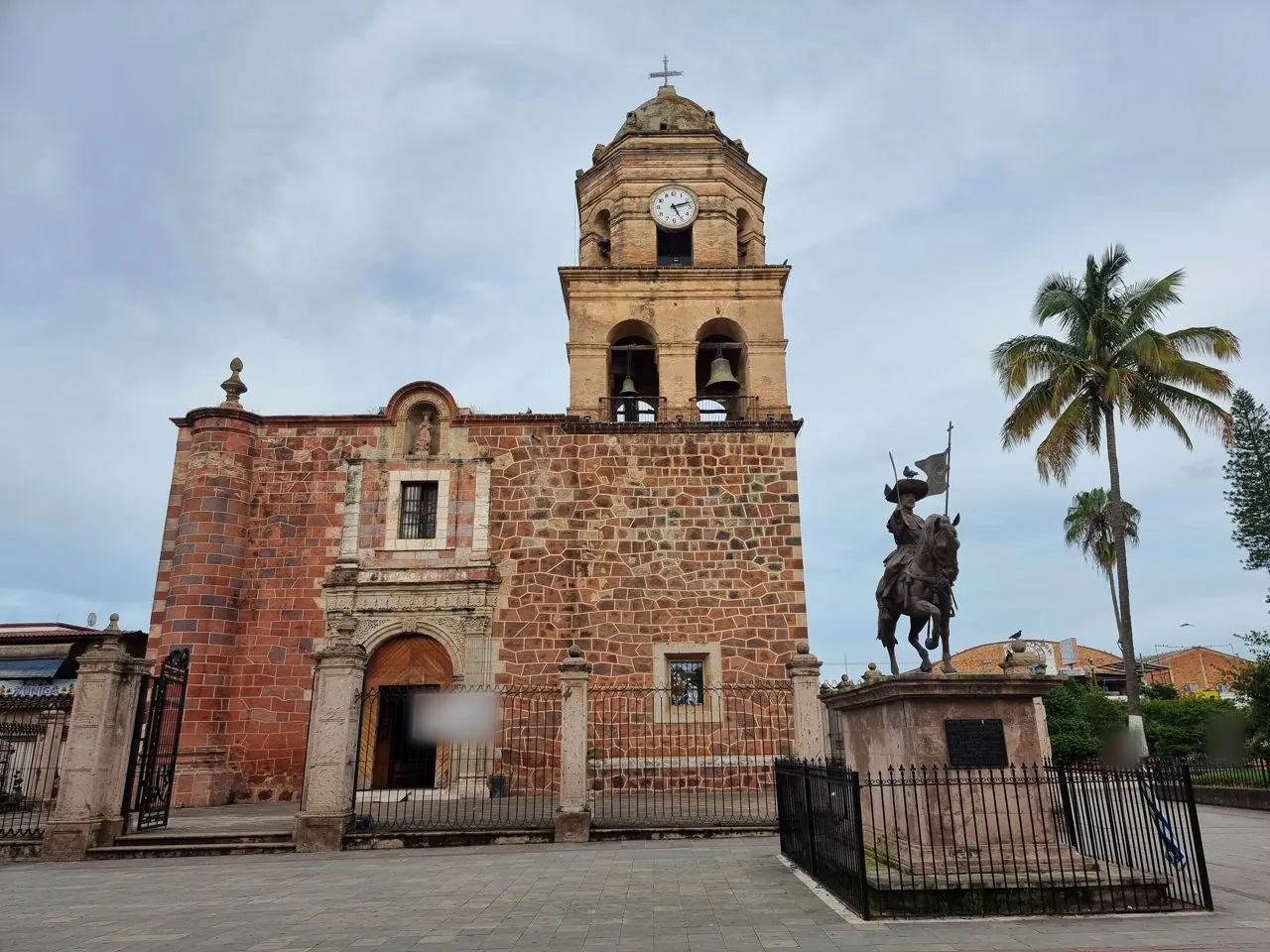 Templo de cantera roja con torre y estatua ecuestre en la plaza de Compostela