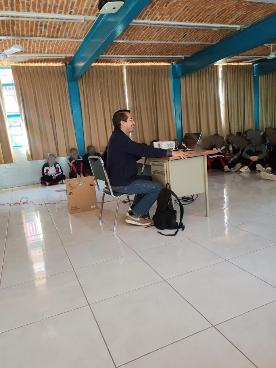 Emilio Andrés sentado al escritorio con estudiantes al fondo